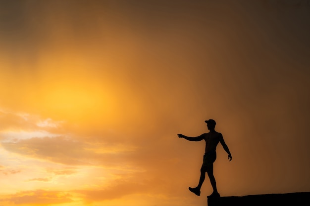 Schattenbild des Mannes, der vom Rand während des dramatischen Sonnenuntergangs tritt