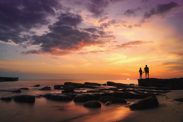 Schattenbild des Paares, das Hände hält und den Sonnenuntergang auf dem Meeresstrand in der schönen Zeit betrachtet.