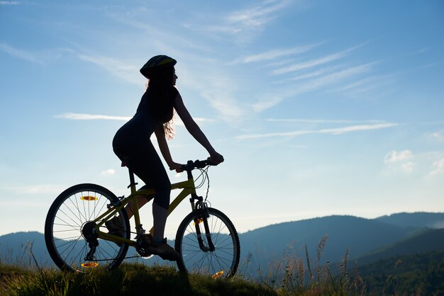 Schattenbild des starken weiblichen Radfahrers, der auf Mountainbike am sonnigen Morgen fährt