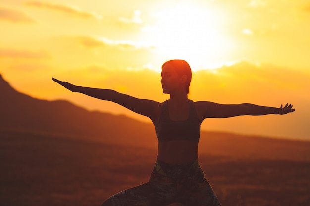 Schattenbild des übenden Yoga oder der pilates der jungen Frau bei Sonnenuntergang oder Sonnenaufgang im schönen Gebirgsstandort.