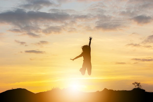Schattenbild einer glücklichen jungen Frau, die am Sonnenuntergang, am Freiheits- und Genusskonzept springt.