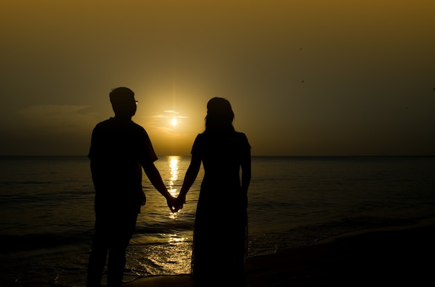 Schattenbild einer jungen Braut und des Bräutigams im Strand auf Sonnenunterganghintergrund