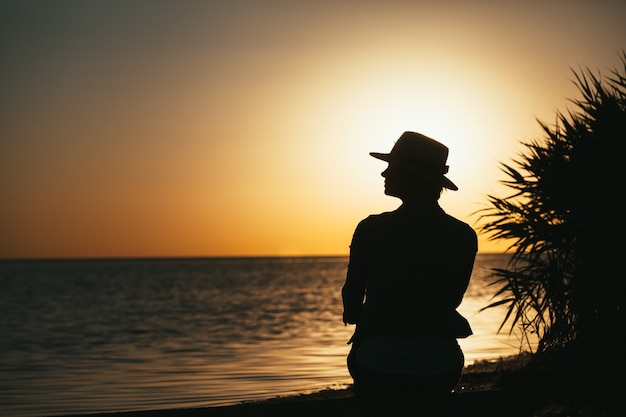 Schattenbild eines Mädchens an der Küste, das einen Sonnenuntergang genießt