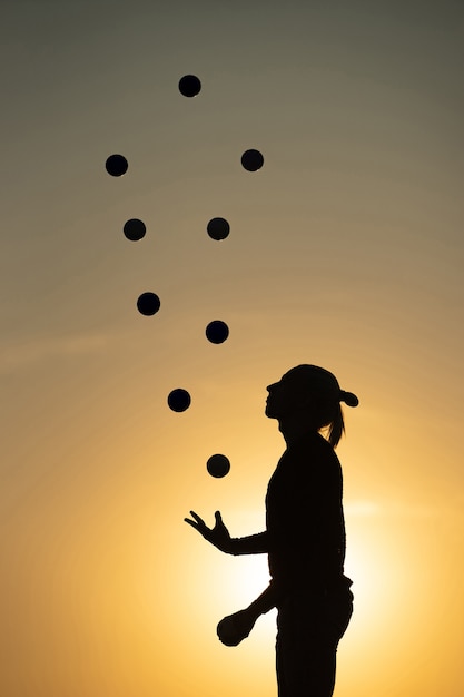 Schattenbild eines Mannes, der bei Sonnenuntergang mit Bällen jongliert.