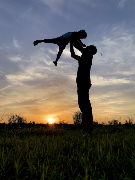 Schattenbild-Vater Carrying Son Against Sky während des Sonnenuntergangs