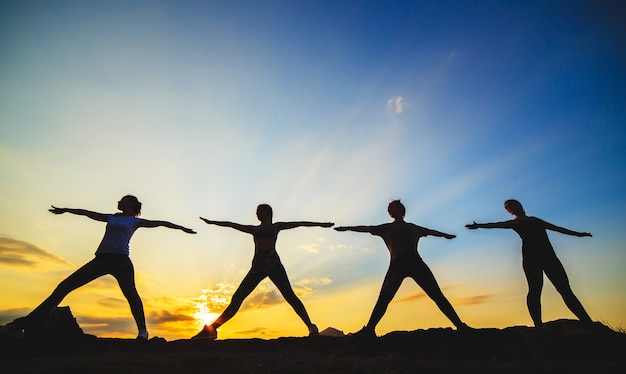 Foto schattenbild von den jungen frauen, die yoga bei sonnenuntergang üben