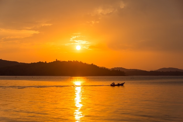 Schattenbildboot des Fischers auf dem Meer bei Sonnenuntergang mit Berg.