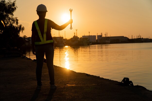 Schattenbilder des asiatischen Fraueningenieurs Schlüssel halten und auf Werft stehen