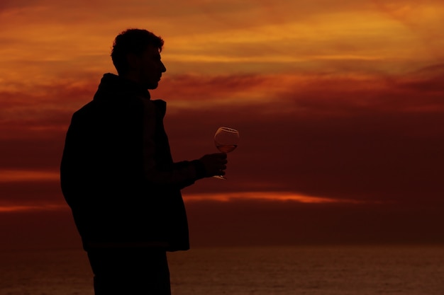 Schattenbilder des Mannes, der ein Glas Champagnerwein bei Sonnenuntergang trinkt