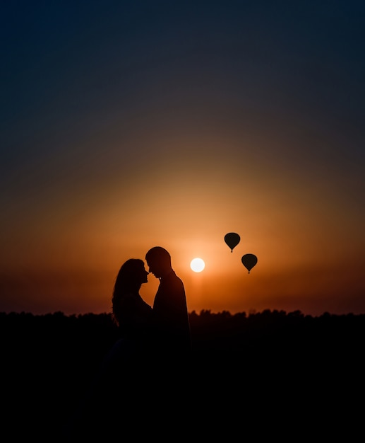 Schattenbilder eines Paares, das vor einem Sonnenuntergang und einer Luft sich umarmt, steigt oben im Himmel auf