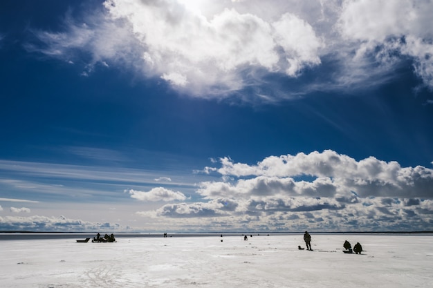 Schattenbilder von den Fischern, die und Schneemobil fischen, im Winter auf dem Eis