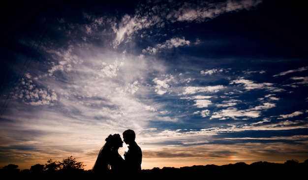 Schattenbilder von den Hochzeitspaaren, die unter dunkelblauem Himmel mit Wolkenreihen stehen