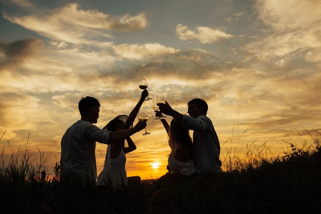 Schattenbilder von Leuten, die auf Feld bei perfektem Sonnenuntergang sitzen.