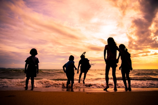 Schattenbildkindergruppe genießen, Meereswellen auf dem Strand im Sonnenuntergang mit schönem twilight Himmel zu spielen