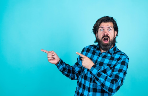 Schau da drüben reifer Kerl mit Schnurrbart im Gesicht, der menschliche Emotionen ausdrückt und mit dem Finger zeigt überraschter Mann im karierten Hemd emotionaler Mann auf blauem Hintergrund brutaler bärtiger Hipster