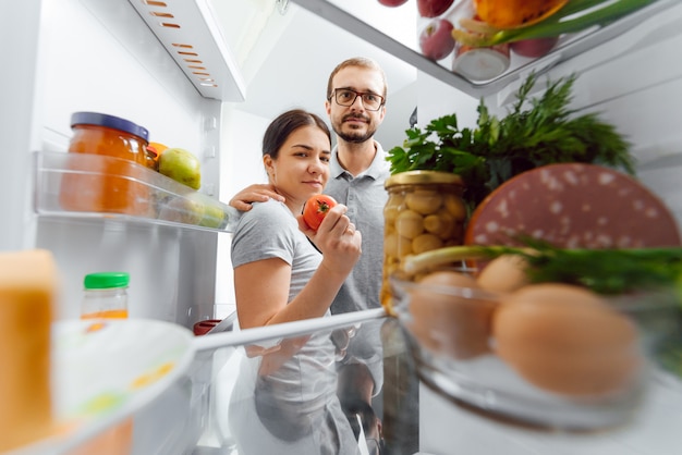 Schau in den Kühlschrank. Junges und erfolgreiches verliebtes Paar schaut in den Kühlschrank und holt eine Flasche Milch aus dem Kühlschrank, während es in der Küche steht und Frühstück macht.