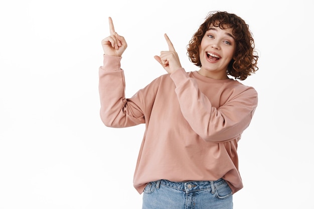 Schau mal rein, klick hier. Lächelndes süßes Mädchen, das mit dem Finger auf die obere linke Ecke zeigt, Top-Werbung, Werbeplatz mit fröhlichem Gesicht zeigt, winkt, dorthin zu gehen, weißer Hintergrund