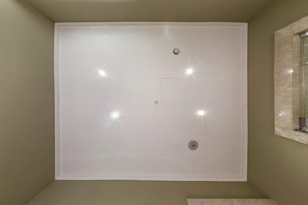 Schauen Sie auf abgehängte Decke mit Halogenspots und Trockenbau mit Brandmeldesensor im leeren Raum in Wohnung oder Haus Spanndecke weiß und komplexe Form