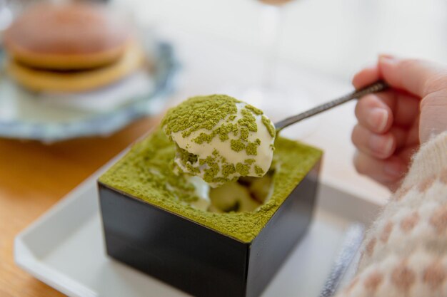 Schaufel des japanischen Matcha-Tiramisu in Holzkiste mit selektivem Fokus von Sake und Matcha-Sirup