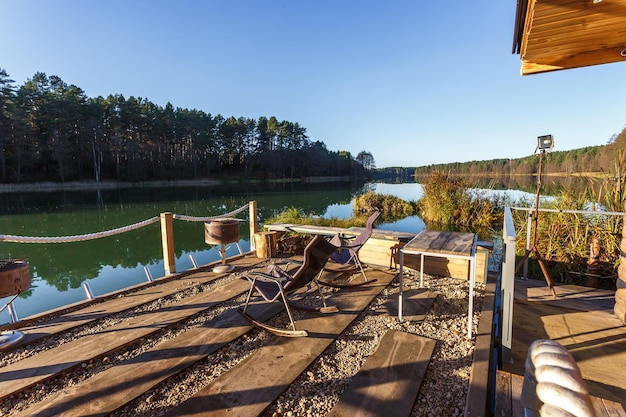 Schaukelstuhl auf einem Holzsteg am See Haus am Wasserrastplatz vor dem Hintergrund einer herbstlichen Landschaft