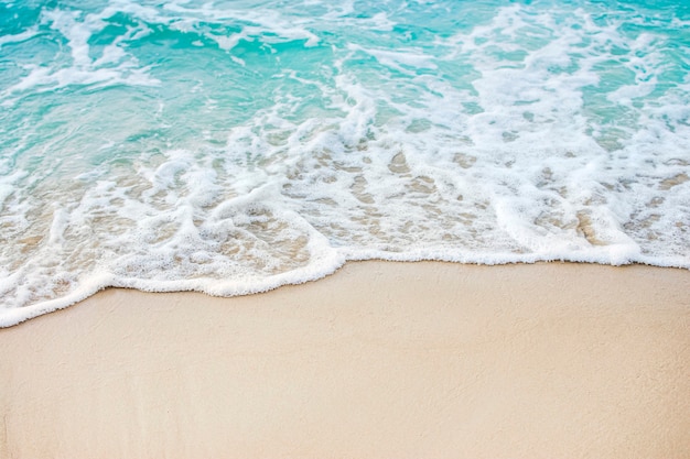 Schaumige Wellen an einem Sandstrand mit blauem Meerwasser an einem tropischen Strand
