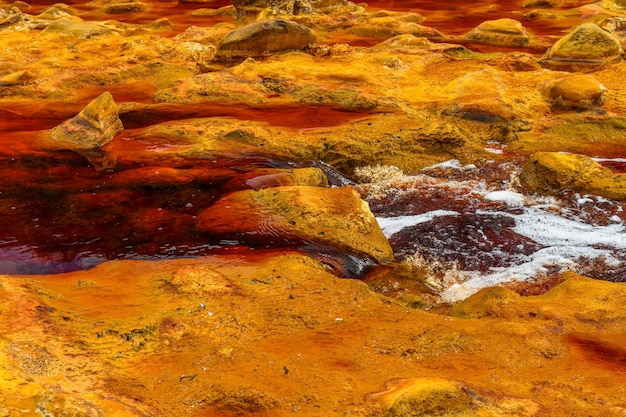 Schaumiges Wasser fließt über die mineralreichen Felsen von Rio Tintos