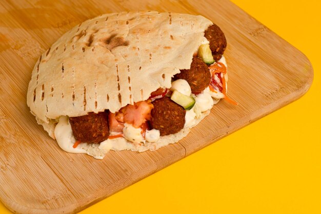 Schawarma mit Falafel auf einer Holzbrettseitenansicht auf gelbem Hintergrund