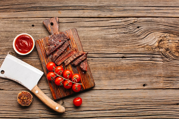 Foto scheibe des gegrillten steaks und der roten kirschtomate auf schneidebrett über holztisch