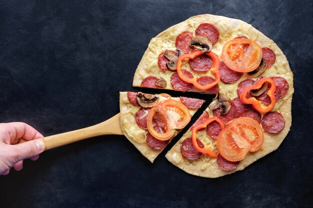 Foto scheibe pizza auf hölzerner spachtel auf schwarzem draufsichtkopienraum