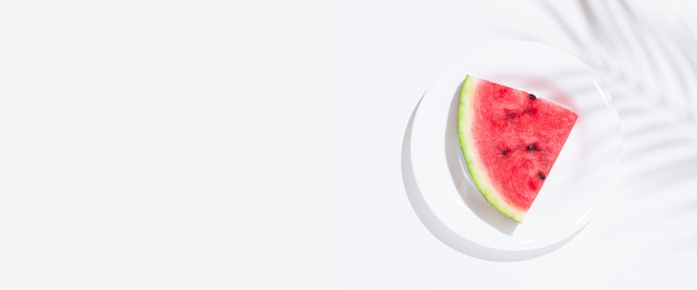 Scheibe Wassermelone auf einem weißen Teller auf einem weißen Tisch Draufsicht flach liegend Banner