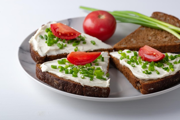 Scheiben Brot mit Hüttenkäse, Zwiebeln und Tomaten auf Platte auf weißem Hintergrund