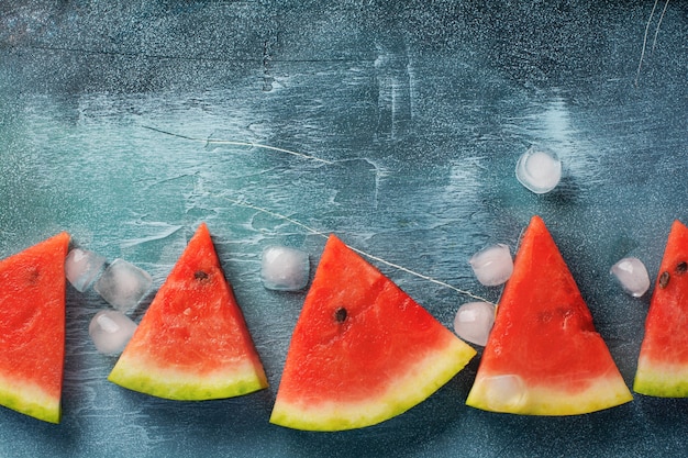 Scheiben der frischen Wassermelone mit Eis auf einem blauen Betontisch. Entgiftung und vegetarisches Konzept. Draufsicht, Kopierraum, Banner