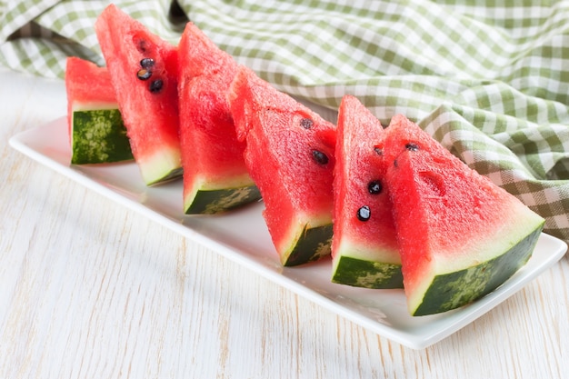 Scheiben der Wassermelone auf dem Teller auf weißem hölzernem Hintergrund.