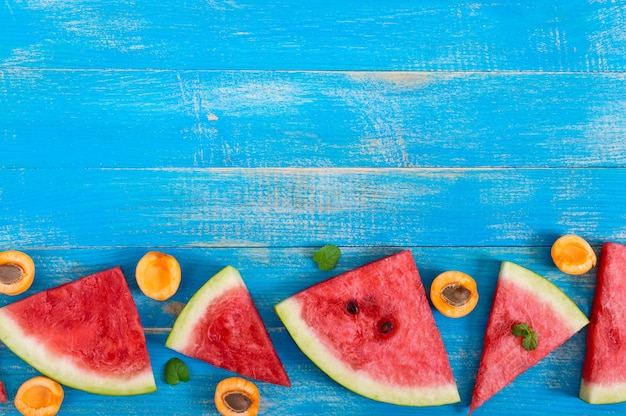 Scheiben einer reifen Wassermelone mit Minzblättern und Aprikose auf blauem Holzhintergrund