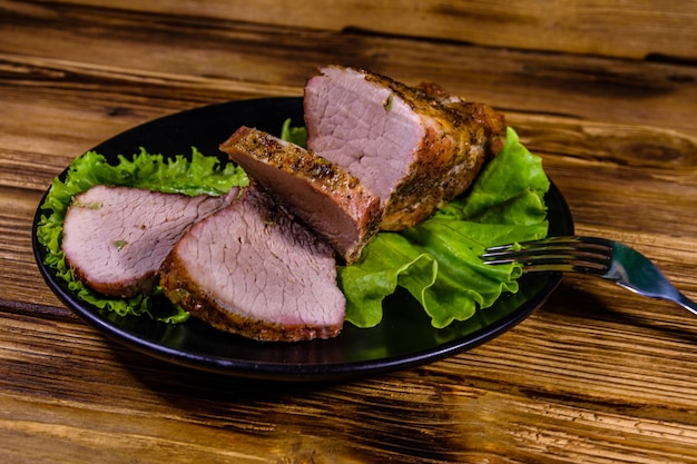 Scheiben gebackenes Schweinefleisch und Salatblätter auf einem schwarzen Teller