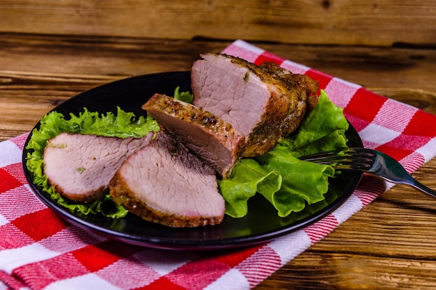 Scheiben gebackenes Schweinefleisch und Salatblätter auf einem schwarzen Teller