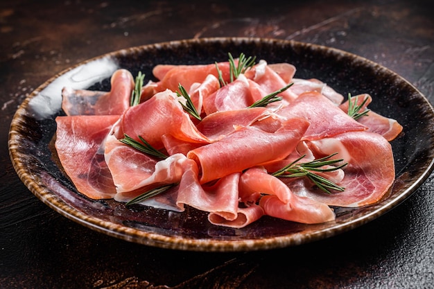 Scheiben Prosciutto Crudo Parma oder Jamon Serrano mit Rosmarin Dunkler Hintergrund Ansicht von oben