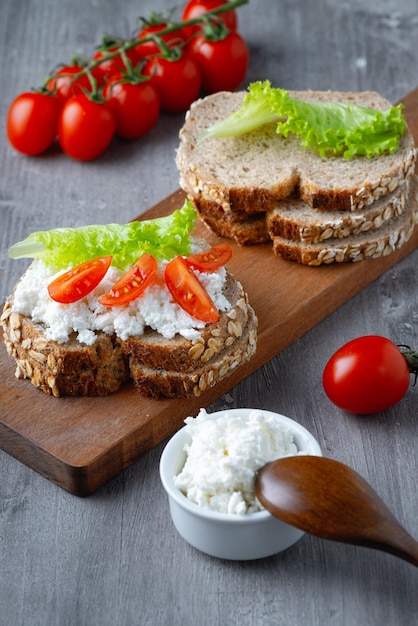 Scheiben Roggenbrot mit Hüttenkäse und Tomaten auf Holzplatte auf grauem Hintergrund