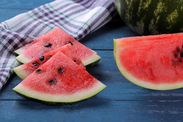 Scheiben rote reife Wassermelone auf einem blauen Holztisch und eine ganze Wassermelone im Hintergrund