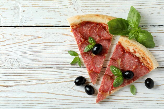 Scheiben Salami-Pizza auf weißem Holzhintergrund