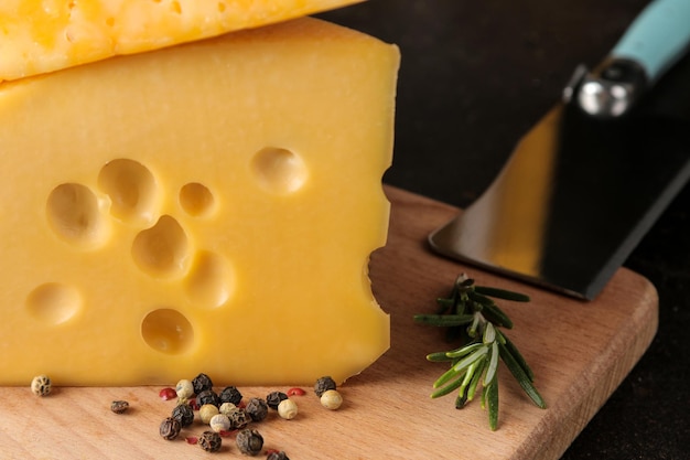 Scheiben von leckerem marmoriertem Käse und Maasdamer Käse mit Gewürzen auf dunklem Hintergrund. Nahaufnahme