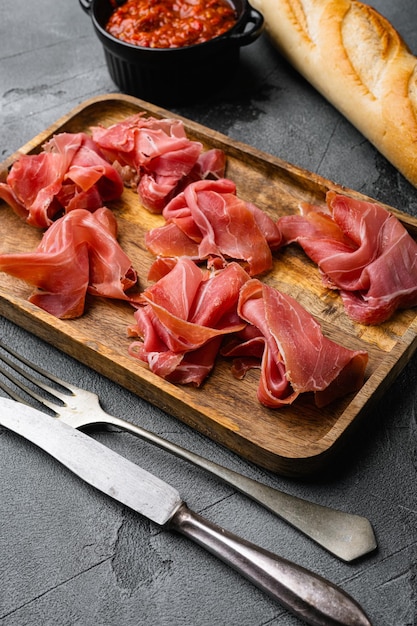 Scheiben von Prosciutto di Parma oder Jamon Serrano auf grauem Steintischhintergrund