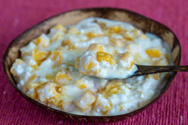 Scheiben von reifen süßen gelben Mangofrüchten mit weißem Hüttenkäsehonig und Sauerrahm in Kokosnussschüssel in der Nähe