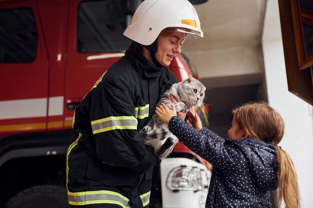 Schenkt dem Besitzer eine Scottish Fold-Katze. Eine Feuerwehrfrau in Uniform ist mit einem kleinen Mädchen zusammen