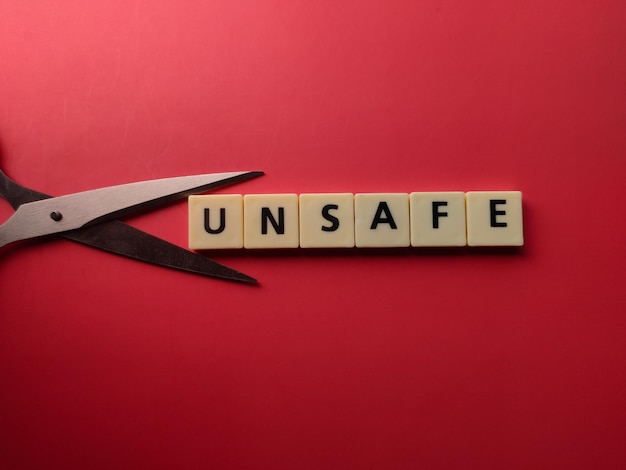 Scheren und Spielzeugbuchstaben mit dem Wort UNSAFE