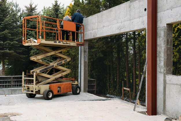 Foto scherenliftplattform mit arbeitern auf einer baustelle, bei der ein betonhaus mit mobilgerät gebaut wird