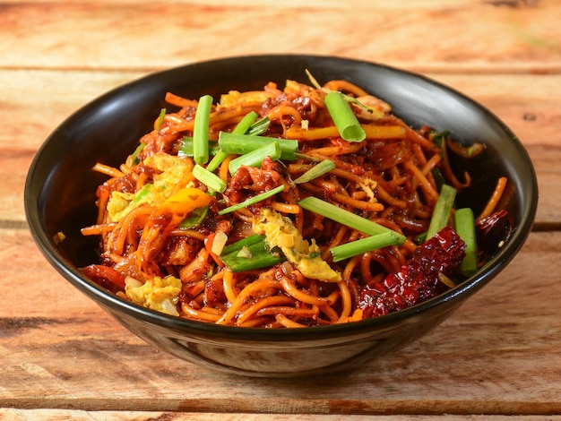 Schezwan Chicken Noodles um popular prato indo chinês feito com macarrão de frango legumes e molho schezwan servido sobre um foco seletivo de fundo de madeira rústico