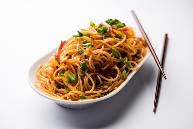 Schezwan-Nudeln oder Gemüse-Hakka-Nudeln oder Chow Mein ist ein beliebtes indo-chinesisches Rezept, das in einer Schüssel oder auf einem Teller mit Holzstäbchen serviert wird. selektiver Fokus