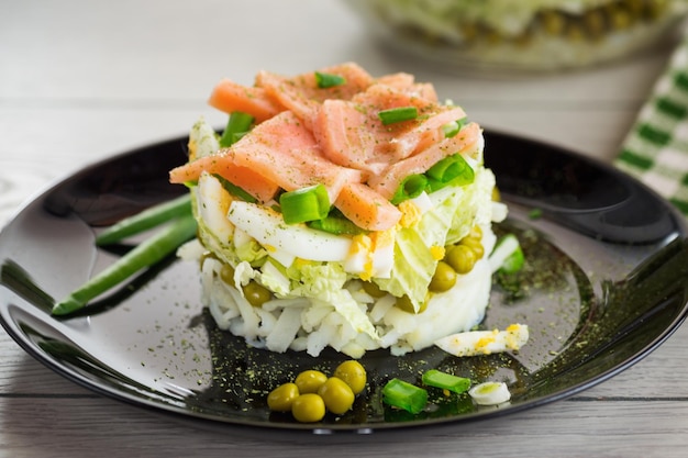 Schichtensalat aus Kohl und anderem Gemüse mit Stückchen roten Fisches auf einem Teller