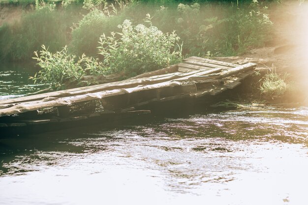 Schiefe schiefe Holzbrücke über kleinen Fluss, aus alten Brettern